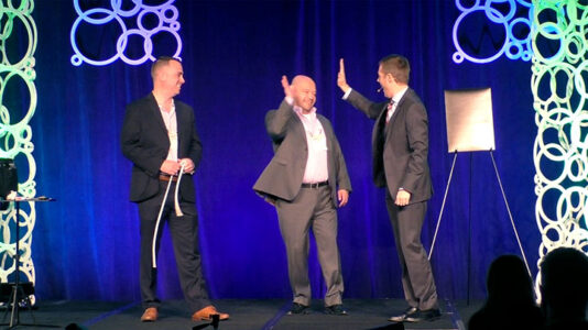 Employees high-five on stage at a conference.